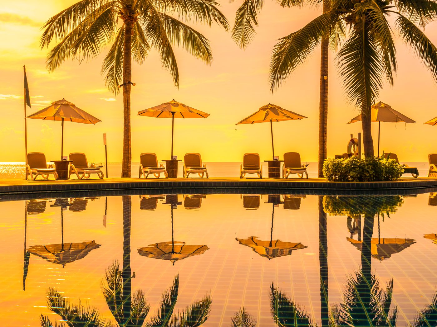 Sun loungers and umbrellas beside a hotel pool at golden hour, palm trees reflected in the water